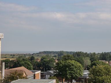 A landscape view over trees and rooftops towards fields and a distant wooded area at Alcombe House in Minehead