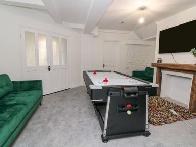 A game room with an air hockey table green sofas and a television above a fireplace at Alcombe House Minehead