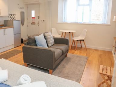 A small living space with a gray sofa two white chairs and table near a window and a small kitchen area at The Mew in Dartmouth