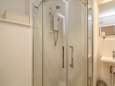 A shower cubicle with glass doors and a white sink with a mirror above in a bathroom at The Mew in Dartmouth