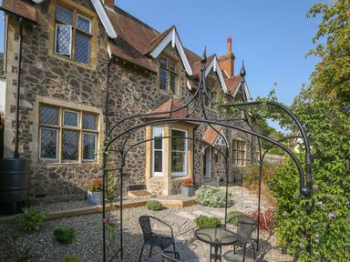 A stone house with leaded glass windows and a small garden seating area at Gable Lodge in Malvern