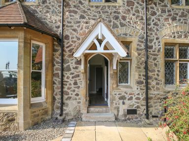 A stone exterior wall with a small arched doorway and three windows at Gable Lodge Malvern
