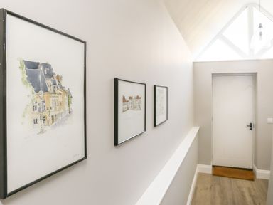 A hallway with three framed paintings on the wall a white door and a brown doormat at Gable Lodge in Malvern