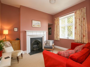 A living room with a fireplace a red sofa a gray chair and a white chair near a window at Gable Lodge in Malvern