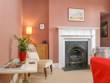 A living room with a fireplace a white chair a red plant pot on a table and a lamp at Gable Lodge in Malvern