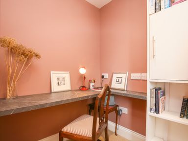 A corner desk with a wooden chair a table lamp framed pictures and a bookshelf at Gable Lodge in Malvern
