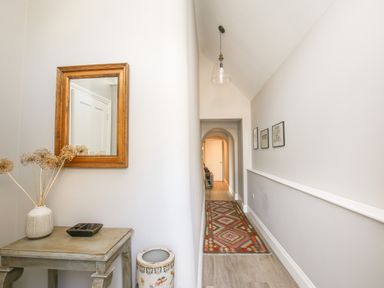 A hallway with a wooden table and mirror a patterned rug and framed pictures at Gable Lodge in Malvern