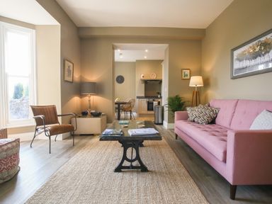 A living room with a pink sofa brown chair coffee table and lamps at Gable Lodge in Malvern
