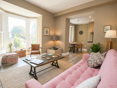 A living room with a pink sofa brown chair glass coffee table and natural fiber rug at Gable Lodge in Malvern