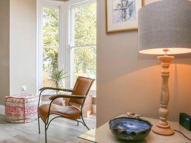 A corner of a room with a brown leather chair near a window and a wooden table lamp on a side table at Gable Lodge Malvern