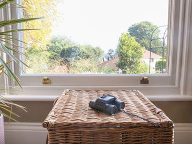 A wicker basket with binoculars on top by a window with a view of trees and houses at Gable Lodge in Malvern
