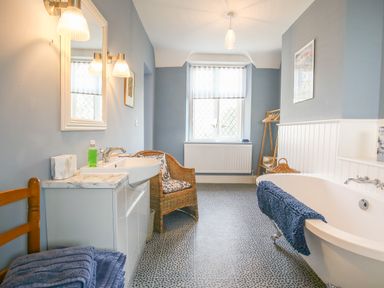A bathroom with a bathtub a wicker chair a sink and a window at Gable Lodge in Malvern
