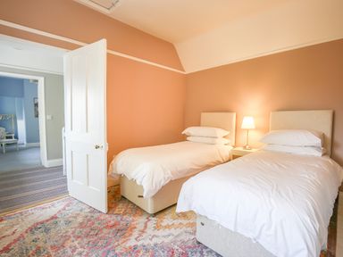 A bedroom with two single beds a nightstand with lamp and an open door showing another room at Gable Lodge Malvern