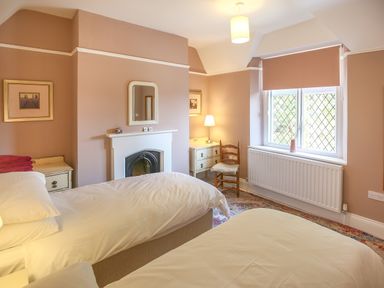 A bedroom with two single beds a window with a blind a fireplace a wooden chair and a small desk with a lamp at Gable Lodge Malvern