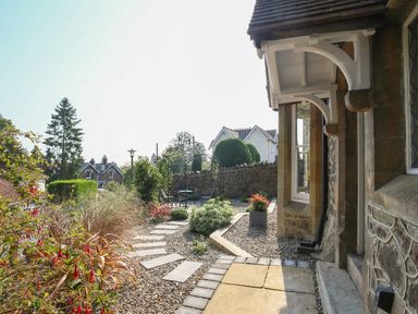 An outdoor garden area with stone pathway metal arch and chairs beside a stone building at Gable Lodge in Malvern