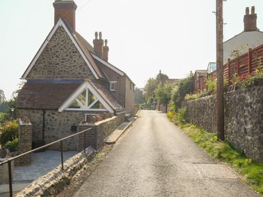 A stone house with a tiled roof beside a narrow paved road with stone walls at Gable Lodge in Malvern