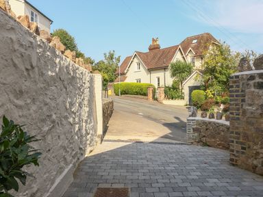 A paved driveway leading to a road with a large house and greenery at Gable Lodge in Malvern