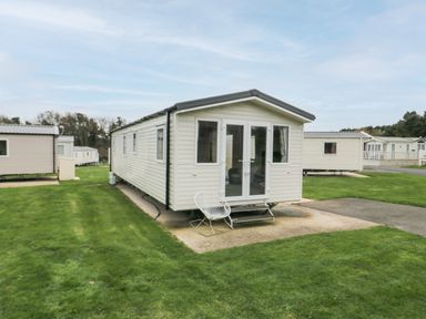 Several beige mobile homes on a grassy plot with one mobile home in the center with a white chair outside at Pines 30 in Cayton