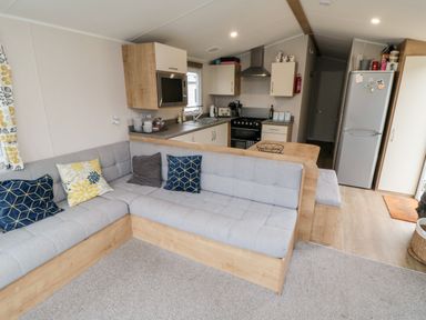 A kitchen and living area with an L-shaped sofa and cushions at Pines 30 in Cayton