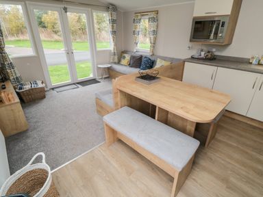 An open plan kitchen and living area with a wooden dining table bench and sofa near windows and glass doors at Pines 30 in Cayton