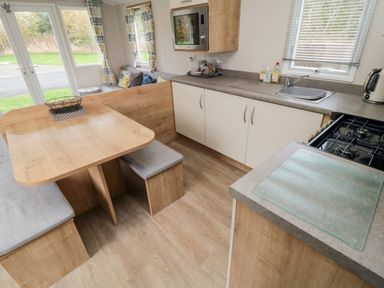 A kitchen area with a wooden dining table and benches a sink stove microwave and sitting area at Pines 30 in Cayton