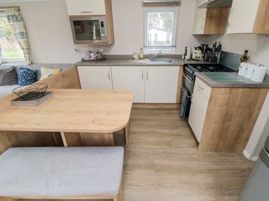 A kitchen with wood and white cabinets a dining table with a bench and a sofa with cushions at Pines 30 in Cayton