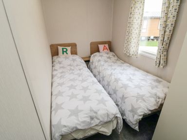 A bedroom with two single beds with star patterned bedding and pillows with letters r and a at Pines 30 in Cayton