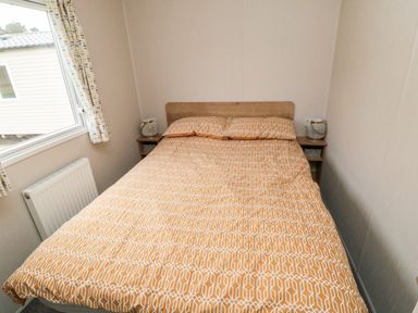 A bedroom with a double bed with patterned orange and white bedding two bedside tables with lamps and a window with patterned curtains at Pines 30 in Cayton