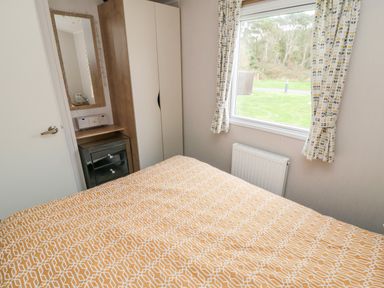 A bedroom with a bed covered in a yellow patterned bedspread a wardrobe a mirror and a window with curtains at Pines 30 in Cayton