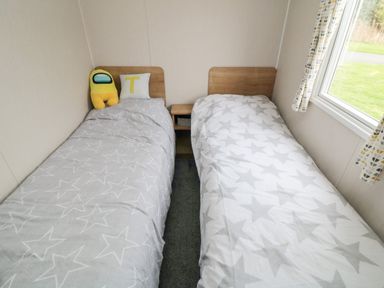 A bedroom with two single beds with star patterned bedding and a window at Pines 30 in Cayton