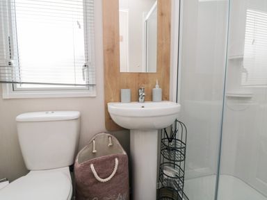 A bathroom with a toilet, a sink with mirror, a laundry basket, and a glass shower enclosure at Pines 30 in Cayton
