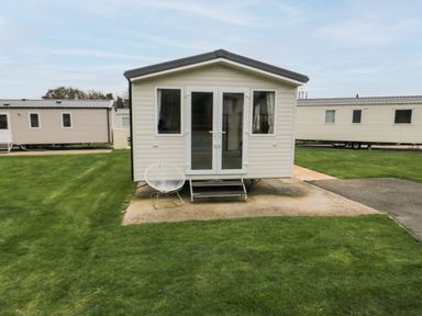 A mobile home with steps and a chair on a concrete slab surrounded by grass at Pines 30 in Cayton