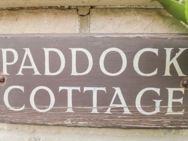 A close up of a wooden sign with the words Paddock Cottage on a wall at Paddock Cottage Nr Malmesbury