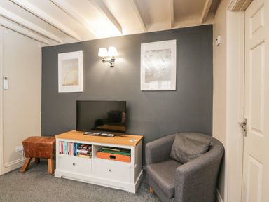 A living room with a gray armchair a TV on a white cabinet and a brown stool at Paddock Cottage Nr Malmesbury