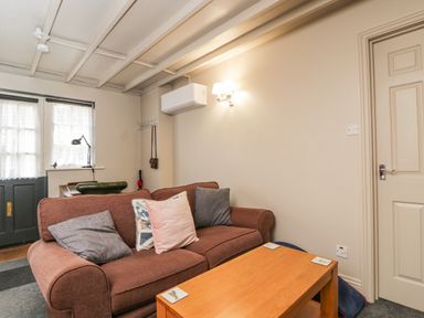 A living room with a brown sofa and cushions a wooden coffee table a door and a window at Paddock Cottage Nr Malmesbury