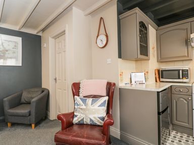 A room with a red leather armchair and pillow near a gray armchair and kitchen cabinets at Paddock Cottage Nr Malmesbury