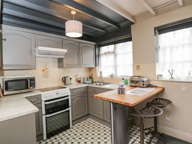 A kitchen with gray cabinets a stove microwave two windows and a wooden countertop with two stools at Paddock Cottage Nr Malmesbury