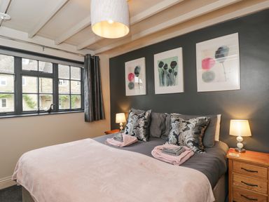 A bedroom with a large bed two bedside tables lamps three framed pictures and a window with curtains at Paddock Cottage Nr Malmesbury