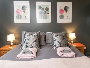 A bedroom with a double bed two bedside tables with lamps and three framed artworks on the wall at Paddock Cottage Nr Malmesbury