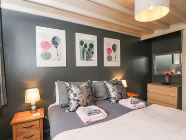 A bedroom with a double bed pillows bedside tables lamps framed artwork and a dresser with a mirror at Paddock Cottage Nr Malmesbury