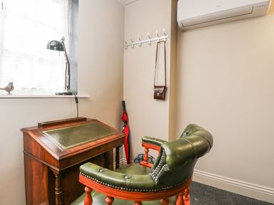 A small room with a wooden desk, green leather chair, desk lamp, umbrella, and wall hooks at Paddock Cottage Nr Malmesbury