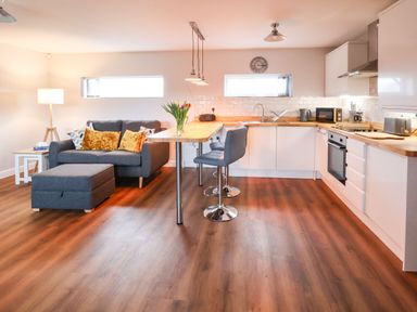An open plan kitchen and living area with a gray sofa with cushions and a matching ottoman at Meols Holiday Lodge in Meols