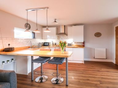 A kitchen with wooden countertops bar stools and a vase of flowers at Meols Holiday Lodge in Meols