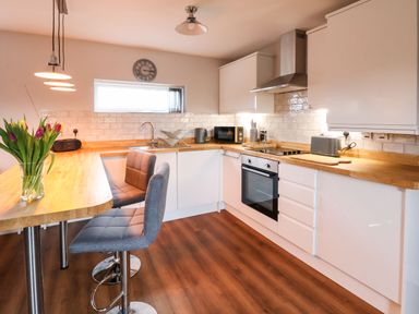 A kitchen with wooden countertops and white cabinets including a sink stove microwave and toaster at Meols Holiday Lodge in Meols