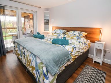 A bedroom with a double bed with patterned bedding and turquoise towels next to patio doors and a small white bedside table at Meols Holiday Lodge in Meols