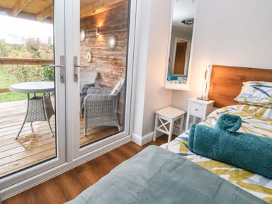 A bedroom with a bed and bedside table next to glass doors leading to an outdoor seating area at Meols Holiday Lodge in Meols