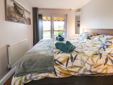 A bedroom with a double bed with patterned bedding teal towels and glass doors leading outside at Meols Holiday Lodge in Meols