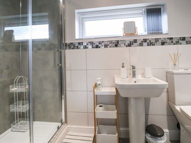 A bathroom with a shower cabin a pedestal sink a toilet and a small storage shelf at Meols Holiday Lodge in Meols