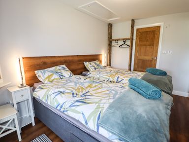 A bedroom with two single beds a wooden headboard bedside tables with lamps towels on the beds a wooden door and a wall-mounted clothes rack at Meols Holiday Lodge in Meols
