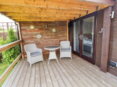 A wooden covered patio with two wicker chairs and a round table at Meols Holiday Lodge in Meols